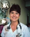 woman stands smiling at the camera wearing a stethoscope around her neck