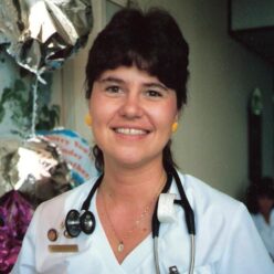 woman stands smiling at the camera wearing a stethoscope around her neck