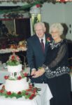 older couple smiles while cutting a white two tier cake