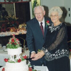 older couple smiles while cutting a white two tier cake