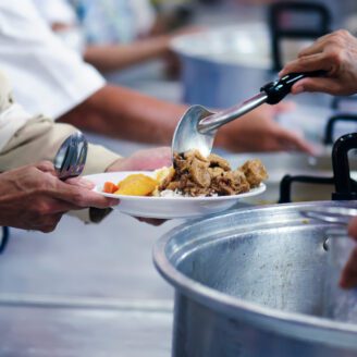 Hands hold a plate while another set of hands spoon food on to the plate.