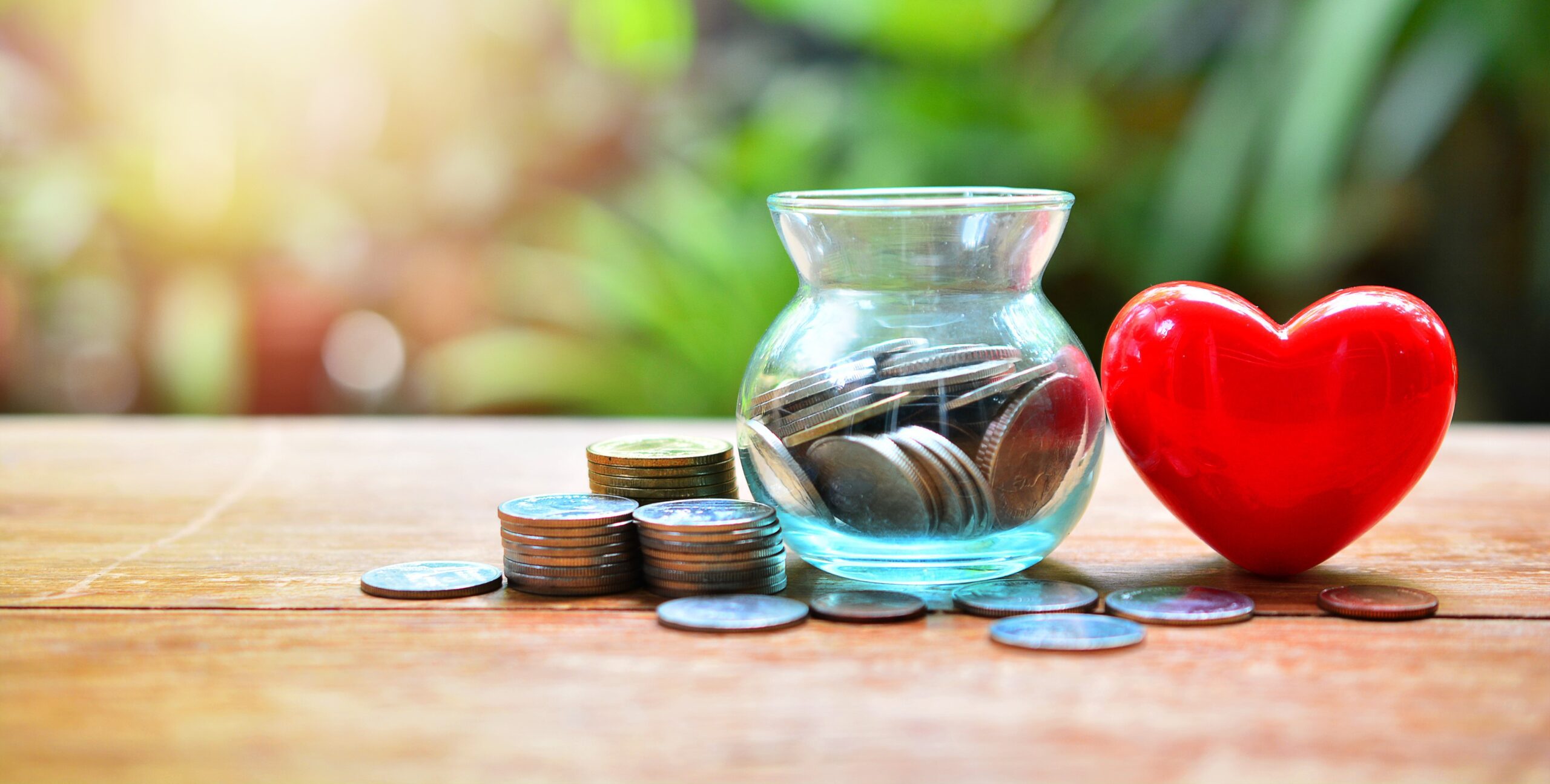 A jar with coins in it sits next to a red heart and other loose coins.