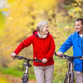 A senior couple walks with bikes through fall foliage.