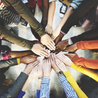 A view from overhead of many diverse hands meeting in the center of a circle.