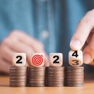 Four wooden dice with the numbers 2024 sit atop stacks of coins.