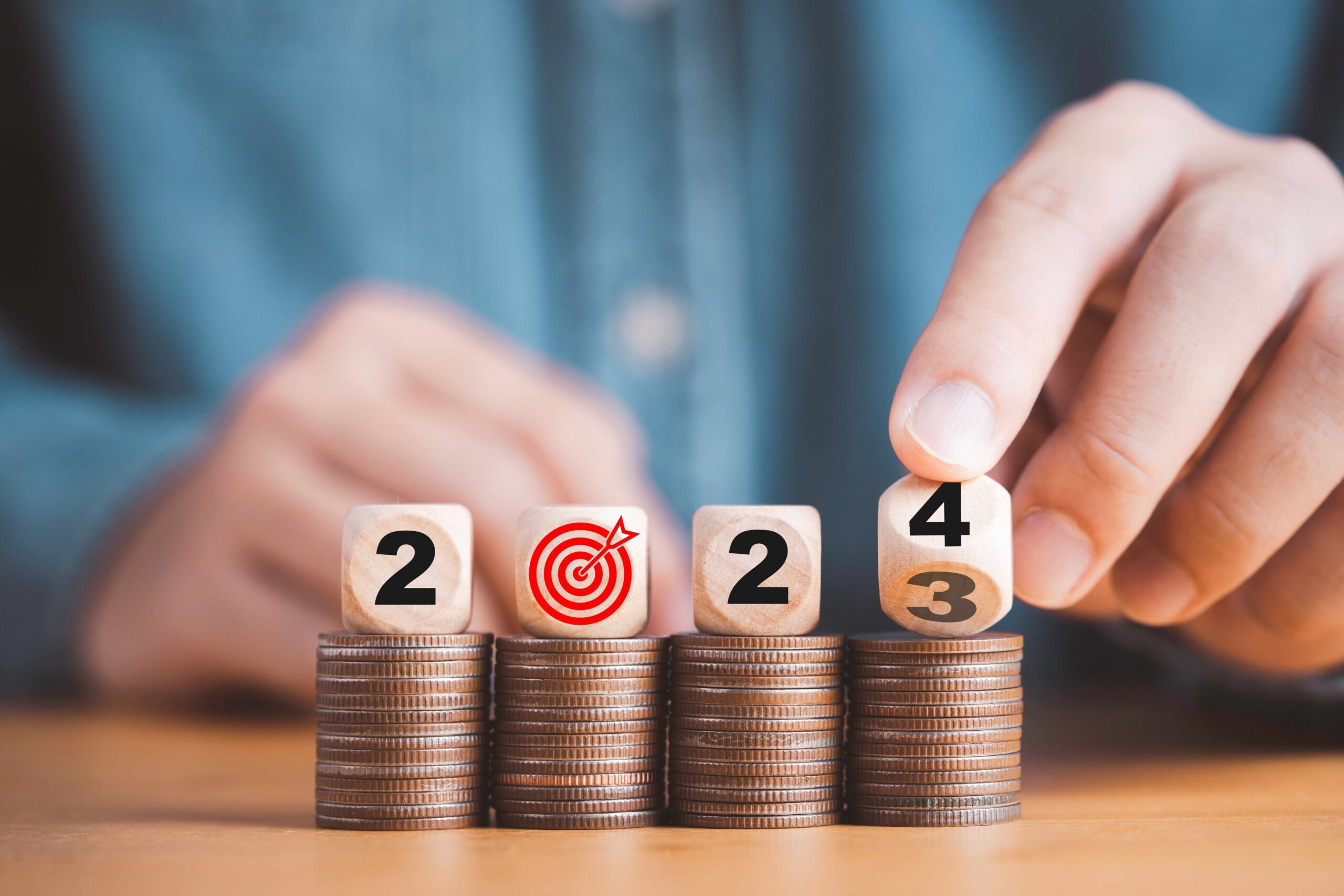 Four wooden dice with the numbers 2024 sit atop stacks of coins. 