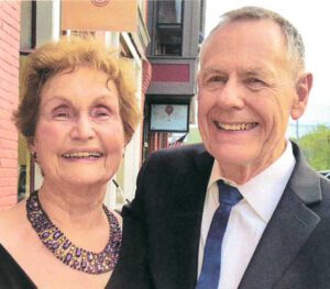 A man and woman stand in front of a building smiling for a photo.