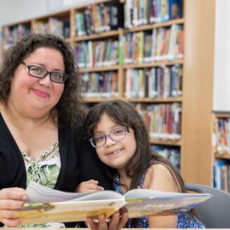 A women and child look at a book in a library.