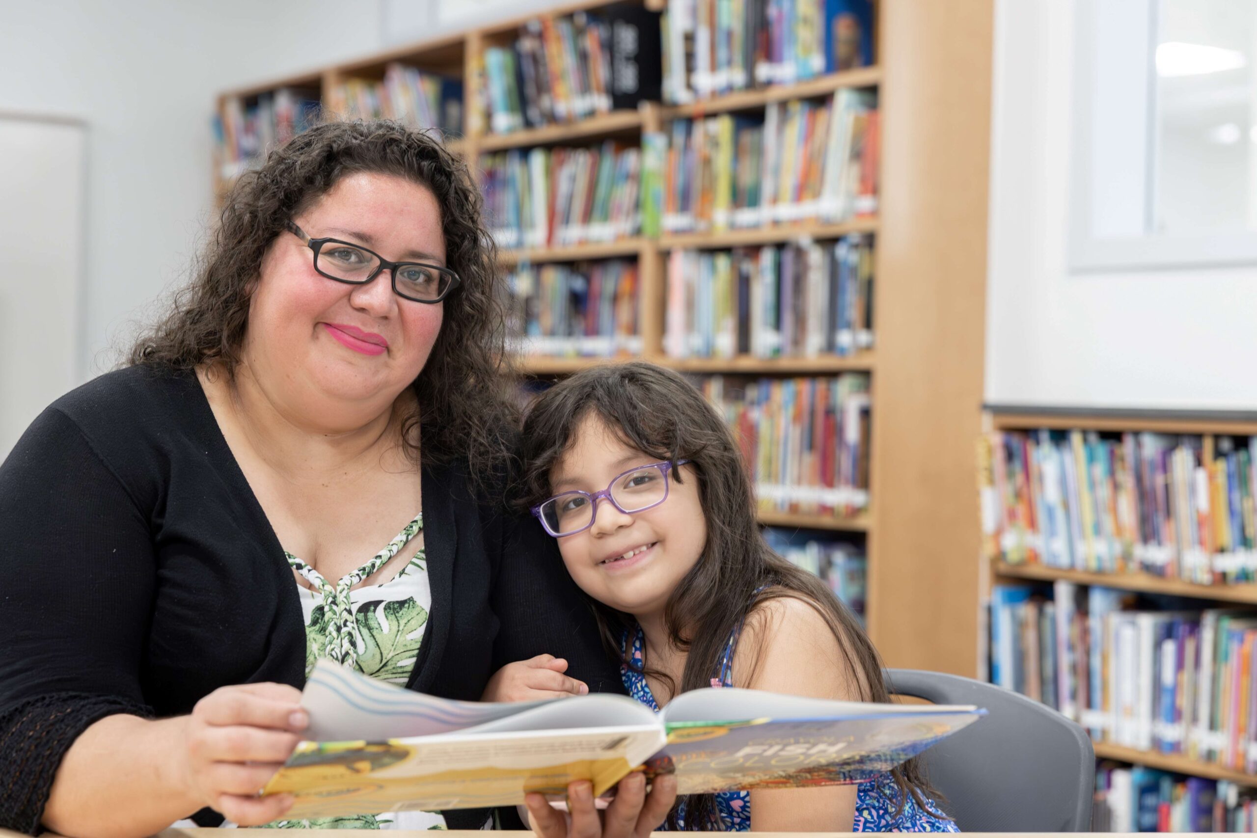 A women and child look at a book in a library. 