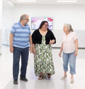 Three adults are talking as they walk down a school hallway. 