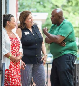 A man speaks with two women on a porch.