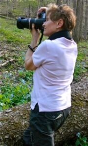 A woman stands taking photos in the wilderness