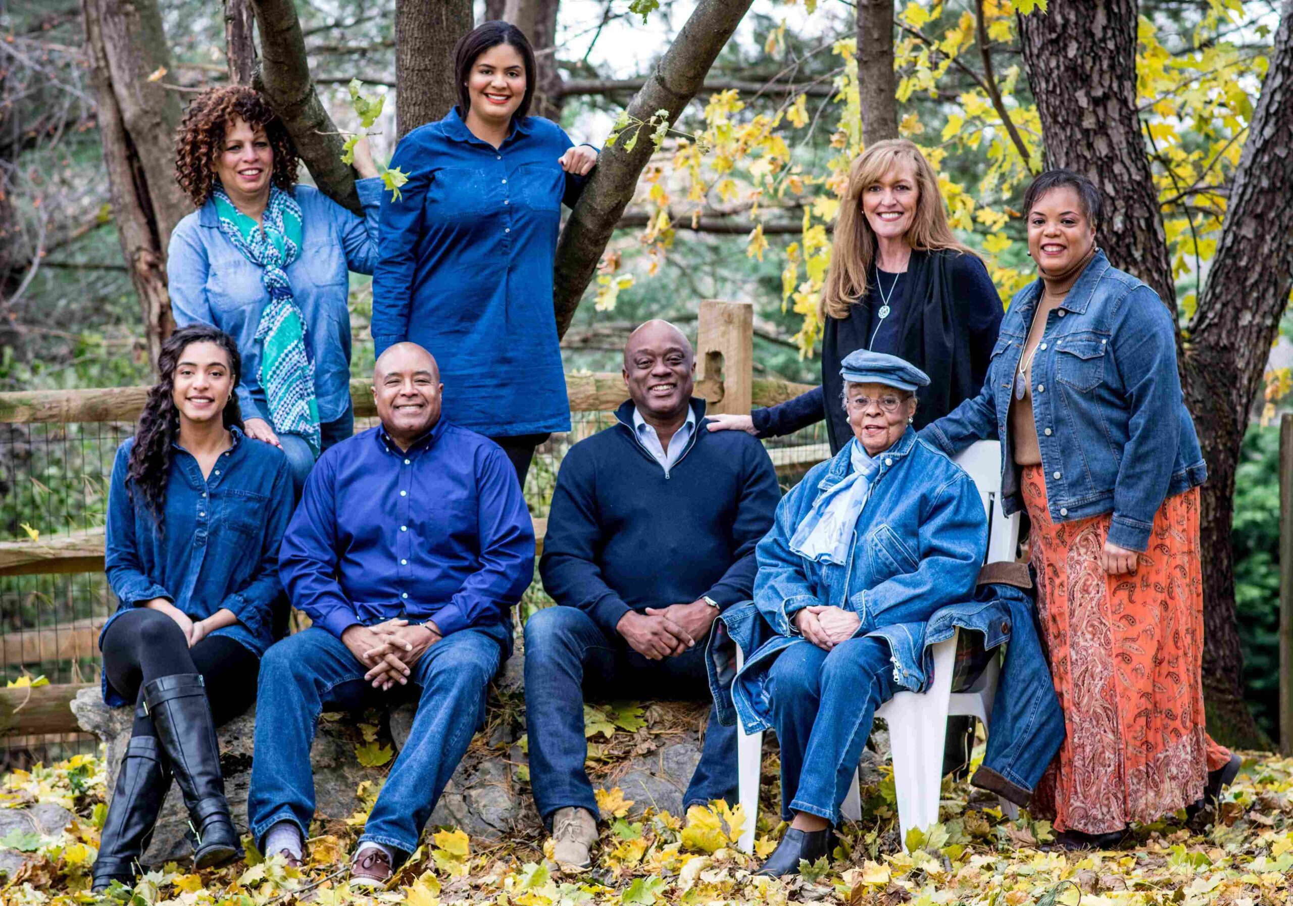 An extended family sits in a wooded area posing for a photo.