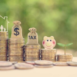 Five stacks of coins with different figures sitting atop including a family, money, taxes, a piggy bank and a plant.