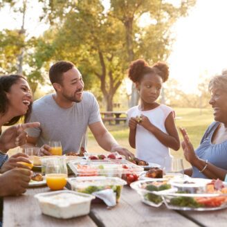 A multi-generational family laughs around a picnic table with healthy food.