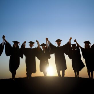 A group of youths wearing graduation attire hold hands while walking.