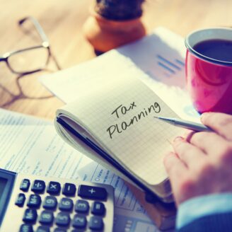 A notepad with "tax planning" written on it is surrounded by a calculator, forms and a cup of coffee.