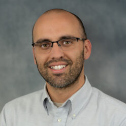 man sits smiling wearing a blue button down shirt