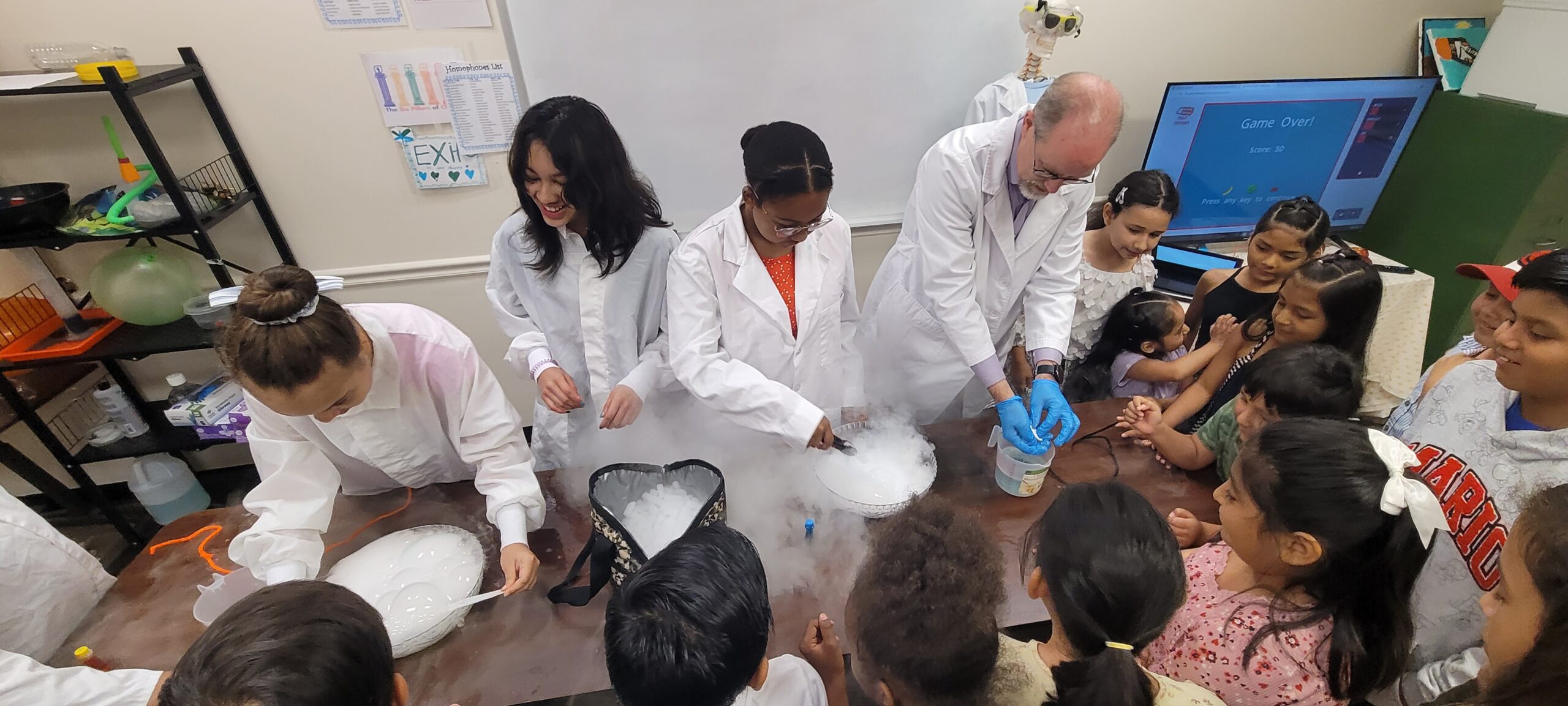 group of children wearing lab coats work around a table