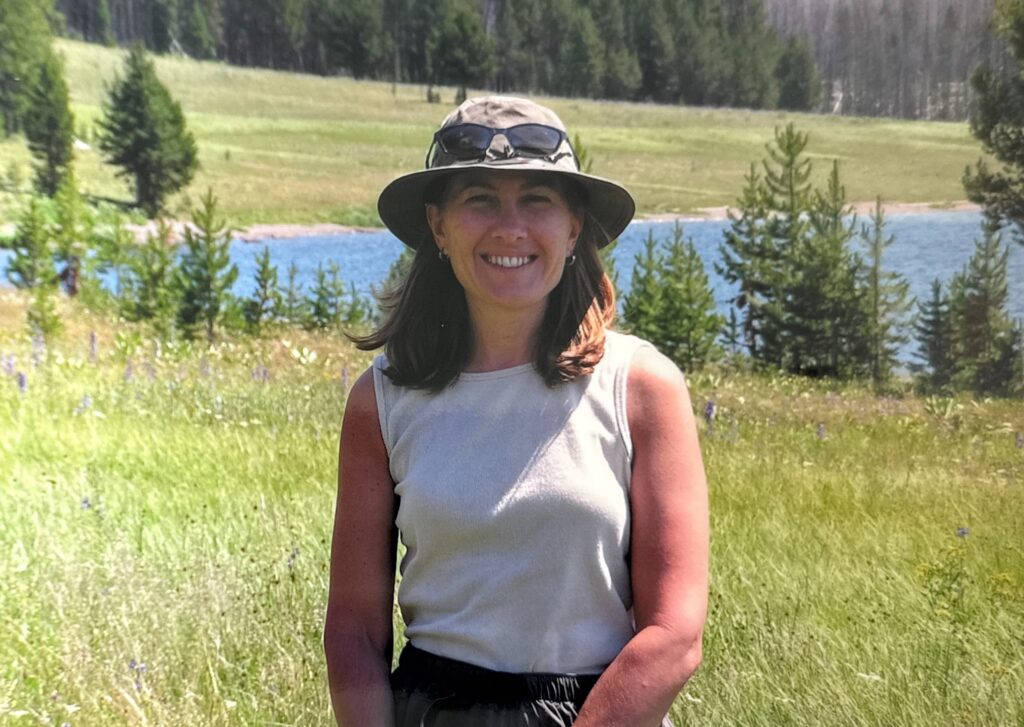 woman stands in a field smiling at the camera