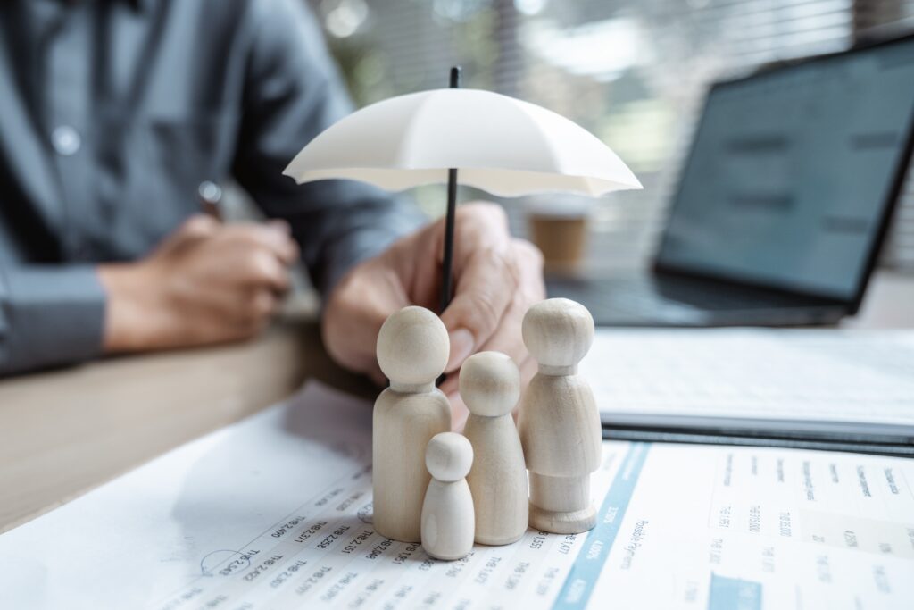 a tiny wooden family sits on a stack of papers with an umbrella held overhead