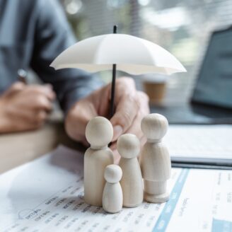 a tiny wooden family sits on a stack of papers with an umbrella held overhead