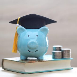 A blue piggy bank wearing a graduation cap sits on top of a textbook