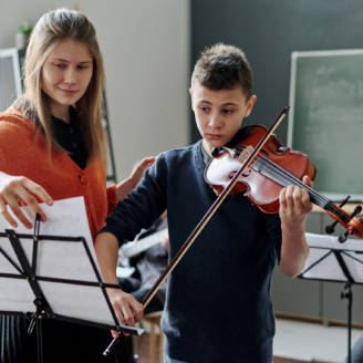 kid playing music with a teacher pointing at the music sheets