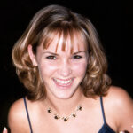 a young woman with short blonde hair looks at the camera with a wide smile
