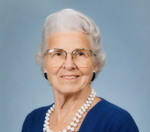 woman with grey hair and glasses sits smiling at the camera