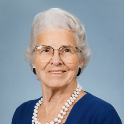 woman with grey hair and glasses sits smiling at the camera